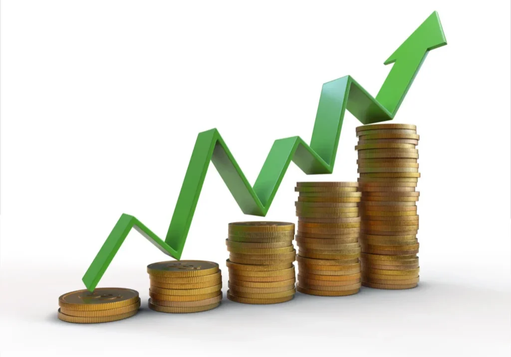 Stacks of gold coins rise from left to right as a green upward arrow climbs above them, symbolizing financial growth, profit, and success.